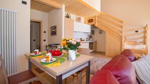A cozy living area with a dining table set for two, a red leather sofa, and a kitchen in the background.