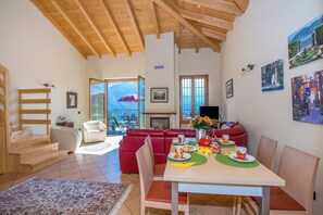 Ampla sala de estar com escada de madeira, sofá vermelho, mesa de jantar com cadeiras e lareira.