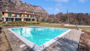 A pool with a stone border, a house with a red roof, and a mountainous backdrop.