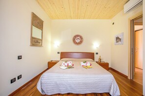 Een verzorgde slaapkamer met een houten plafond, een bed met een wit dekbed, nachtkastjes met lampen en een wandklok.