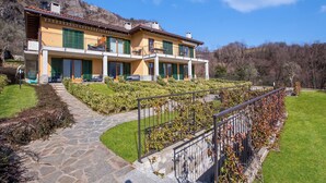 A two-story house with a stone pathway leading to the entrance, surrounded by well-maintained hedges and a mountain backdrop.
