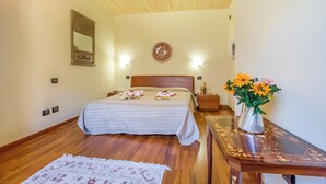 A bedroom with a wooden ceiling, a bed with a headboard, bedside lamps, a nightstand, a vase with flowers, and a patterned rug.