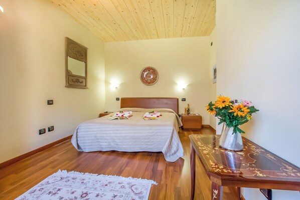 Une chambre avec un plafond en bois, un lit avec une tête de lit, des lampes de chevet, une table de chevet, un vase avec des fleurs et un tapis à motifs.