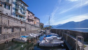 A marina with boats docked along a stone wall, overlooking a body of water with mountains in the background. - Colonno Panoramica (Colonno)