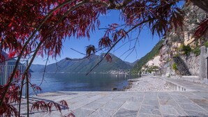 A stone-paved waterfront promenade with a view of a lake and mountains in the background. - Colonno Panoramica (Colonno)