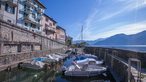A marina with boats docked along a stone wall, a clear sky, and mountains in the background. - Villa Luminosa (Pianello del Lario)