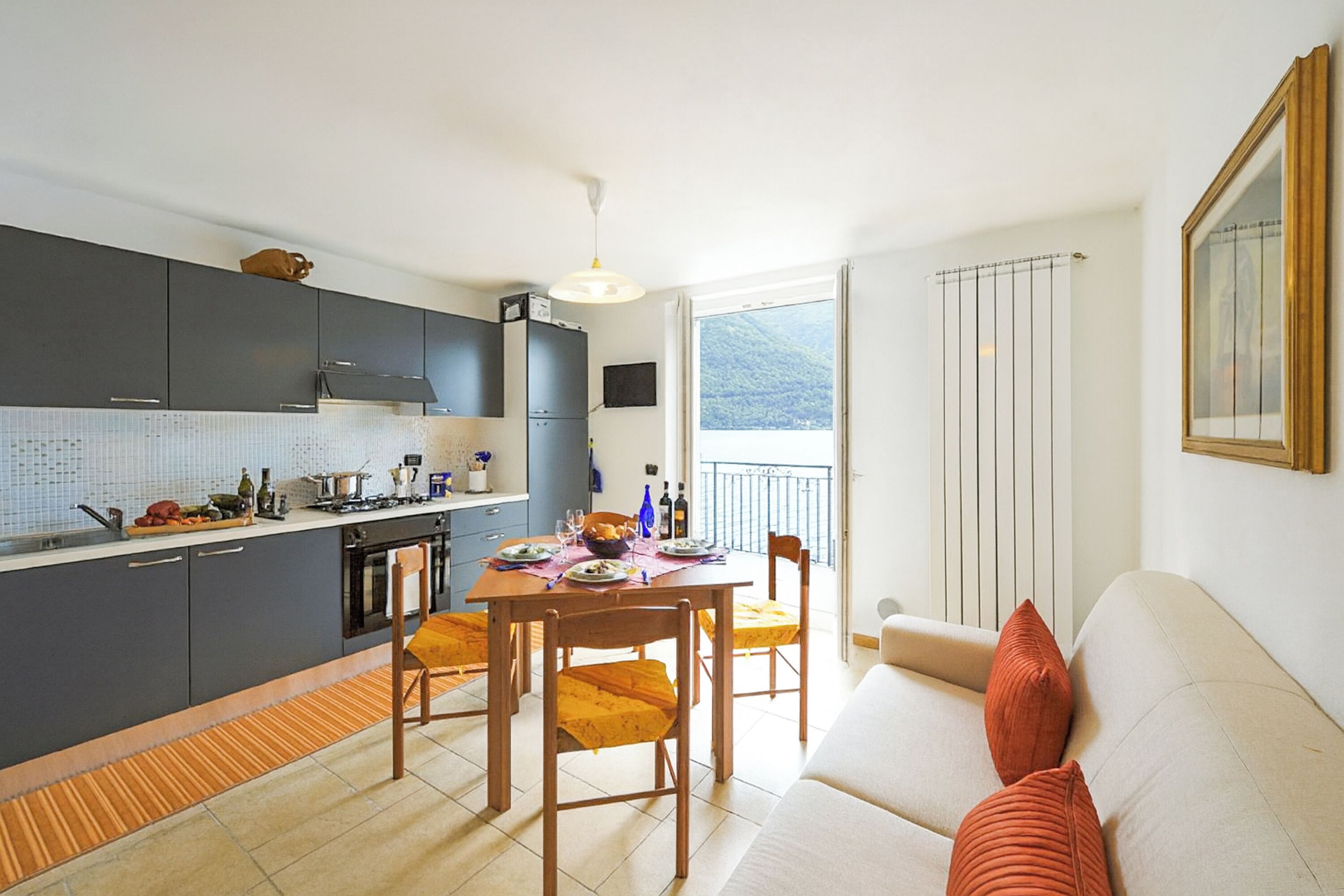 A modern kitchen with dark cabinets, a dining table, and chairs. There is a balcony with a view of the mountains.