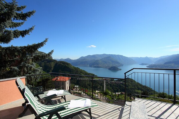A balcony with two striped lounge chairs, a small building, and a view of a lake surrounded by mountains. - Villetta Belvedere Perledo (Perledo)