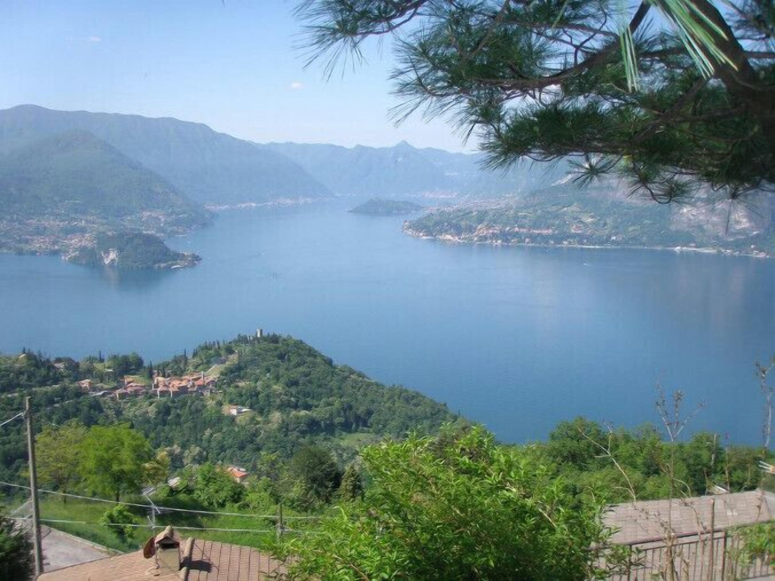 A panoramic view of a lake surrounded by mountains and greenery, with a clear sky.