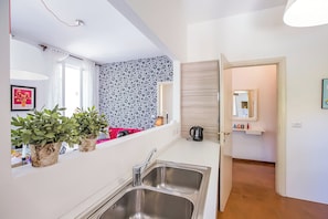 Una cocina moderna con un lavamanos doble, plantas en macetas, un espejo y vistas al cuarto contiguo.