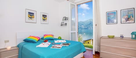 Un dormitorio con cama, cómoda, mesita de noche, ventana con vistas y cuadros en la pared.