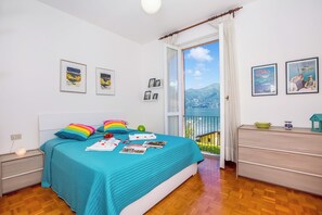 Un dormitorio con cama, cómoda, mesita de noche, ventana con vistas y cuadros en la pared.