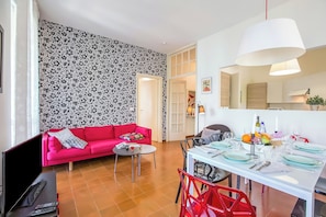Una sala de estar con un sofá rojo, una mesa de comedor preparada para seis personas y una zona de cocina al fondo.