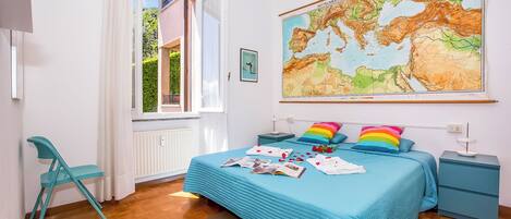 A bedroom with a bed, a map on the wall, a chair, and a nightstand.