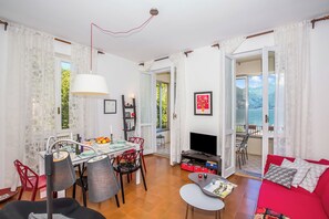 Un comedor con una mesa, sillas y un televisor. Hay un sofá rojo y una ventana con vistas.