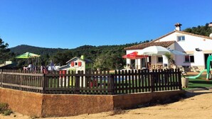 Un espace extérieur clos, comprenant une aire de jeux, une petite maison et un bâtiment plus grand doté d’un patio.