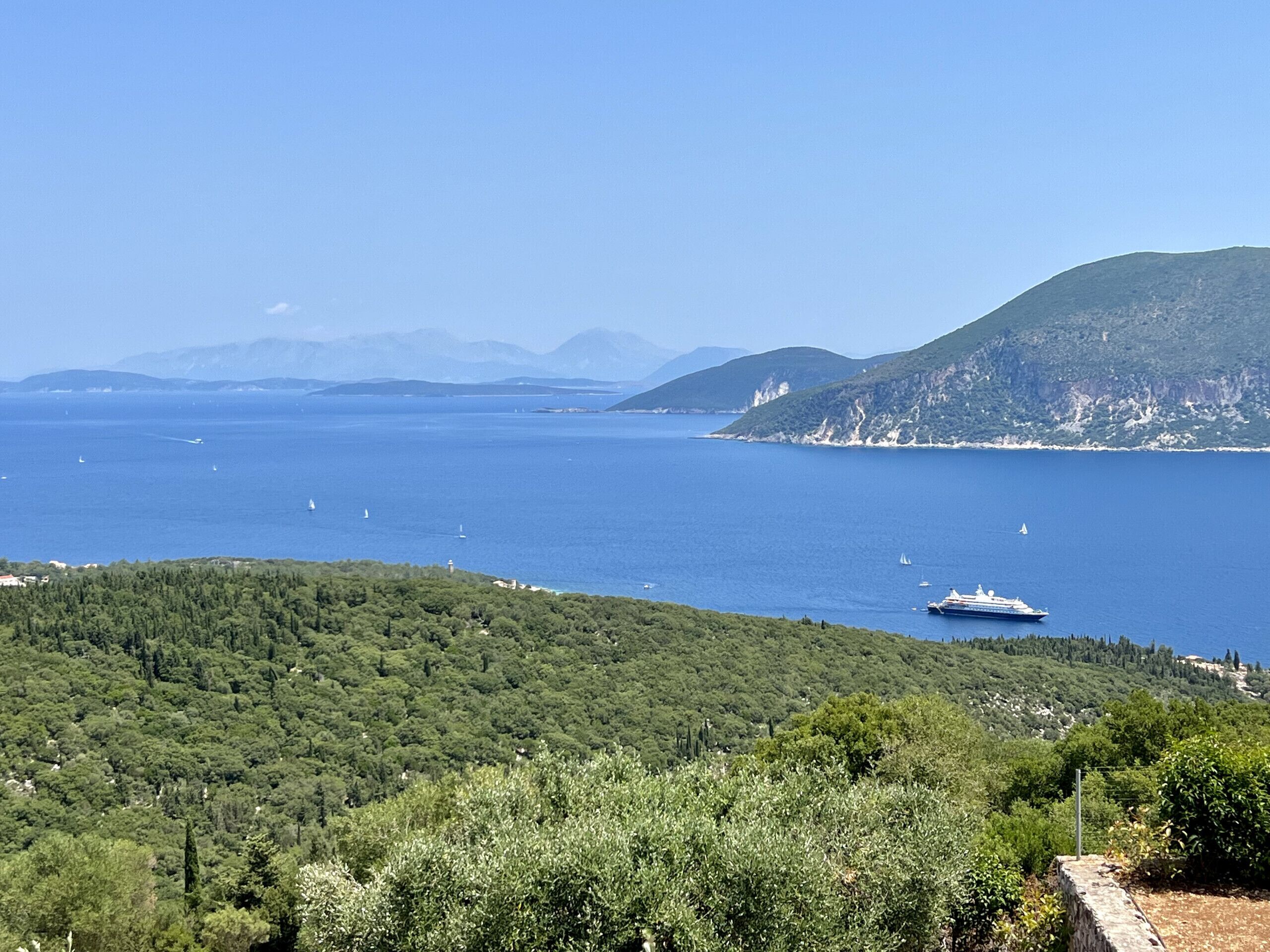 Paesaggio costiero con un'ampia distesa d'acqua, una nave da crociera e montagne sullo sfondo.