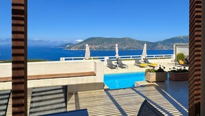Eine Terrasse mit Pool, Liegestühlen und Sonnenschirmen mit Blick auf die Küste.