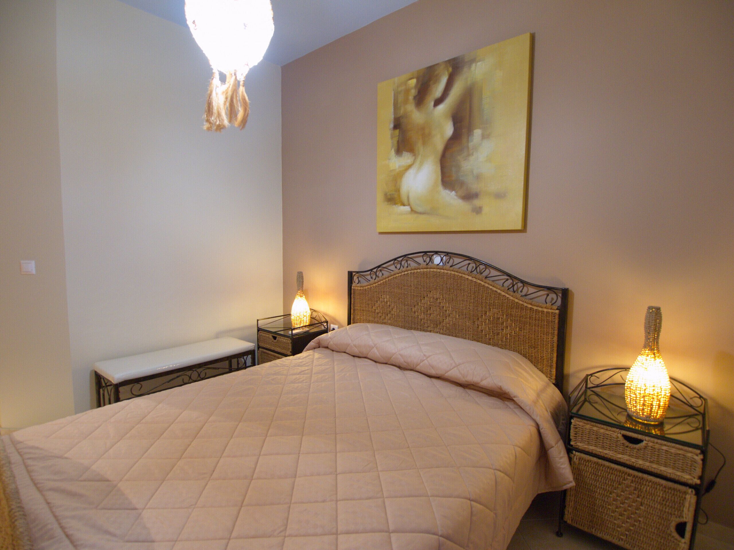 A bedroom with a bed, bedside lamps, a bench, and a wall-mounted painting.