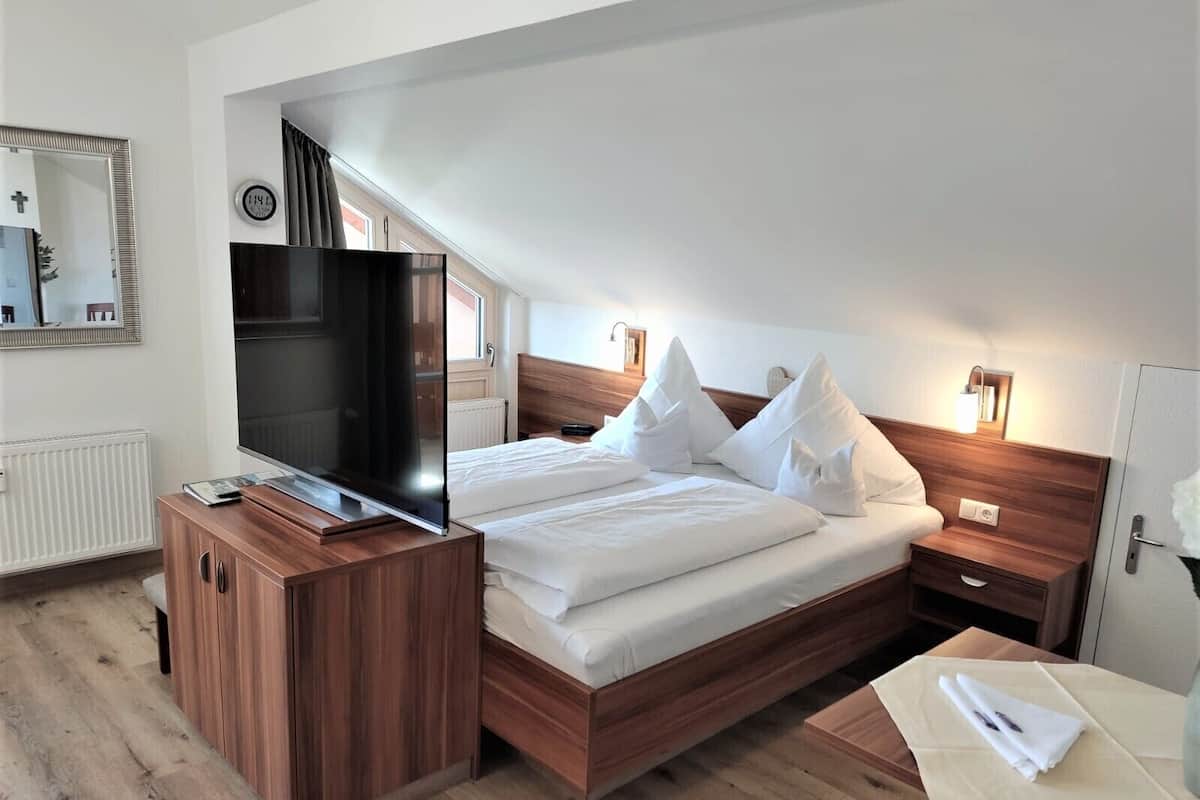 A modern hotel room with a wooden bed, a flat-screen TV, a bedside table, and a nightstand.