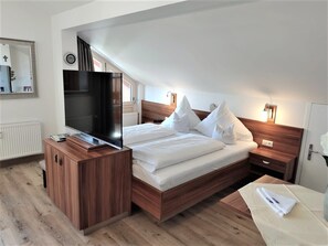 A modern hotel room with a wooden bed, a flat-screen TV, a bedside table, and a nightstand.