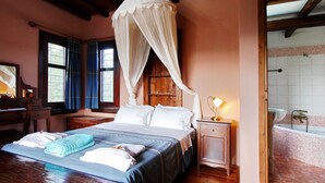A bedroom with a four-poster bed, a nightstand with a lamp, a wooden desk, and a window with curtains. - Villa Galania (Armeni)
