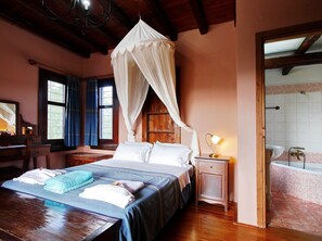 Een slaapkamer met een hemelbed, een nachtkastje met een lamp, een houten bureau en een raam met gordijnen.