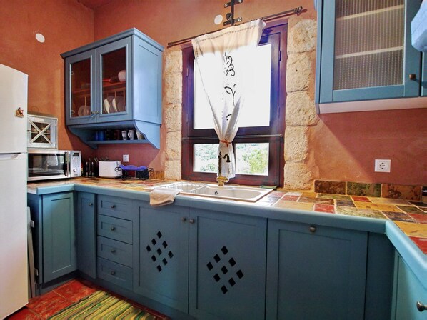 Een keuken met blauwe kastjes, een magnetron, een spoelbak en een raam met gordijn.