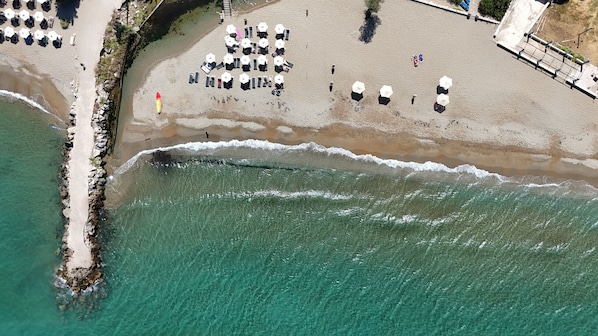 Luchtbeeld van een strand met parasols en ligbedden, klaar om te zonnen.