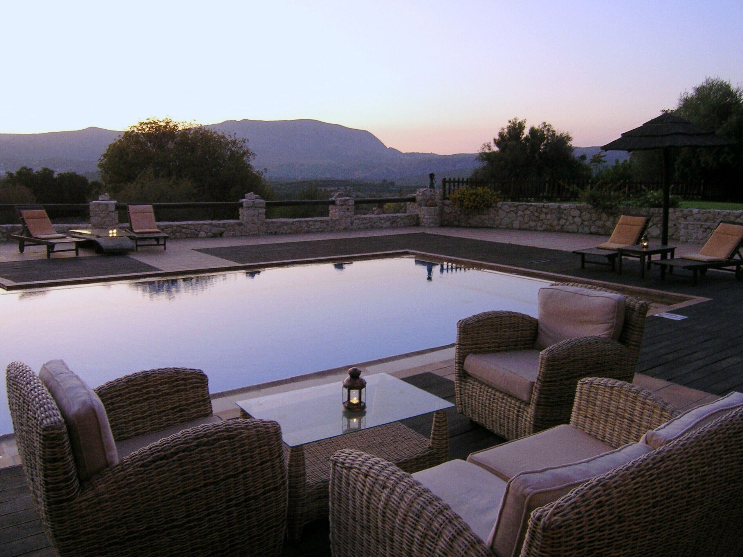 A pool area with wicker furniture and a stone wall.