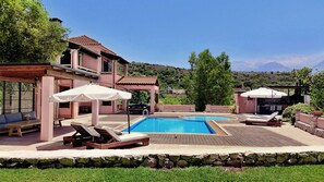 A pool area with lounge chairs and umbrellas, surrounded by a stone wall and greenery. - Villa Galania (Armeni)