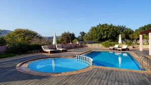 A pool area with two separate pools, lounge chairs, and umbrellas. - Villa Galania (Armeni)