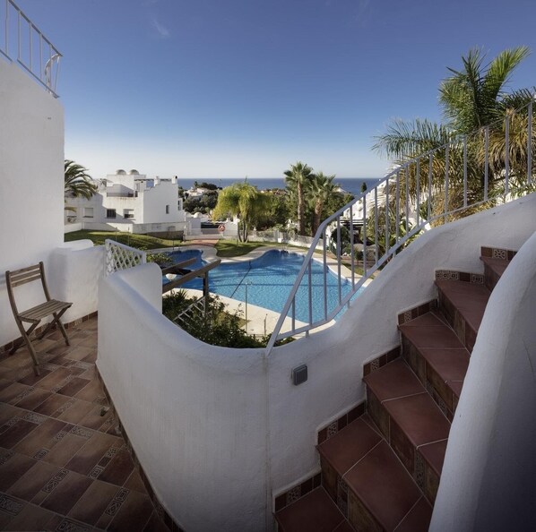 Zona de piscina con escalones que bajan al agua, rodeada de muros blancos y palmeras.