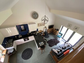 Eine moderne Küche mit schwarzem Arbeitsplatz, weißen Schränken und einer blauen Spritzschutzwand. Es gibt einen Essbereich mit einem schwarzen Teppich und einer Couch.