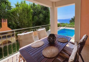 Un balcone con vista sul mare, una piscina e un tavolo con sottopiatti intrecciati e cuscini a righe.