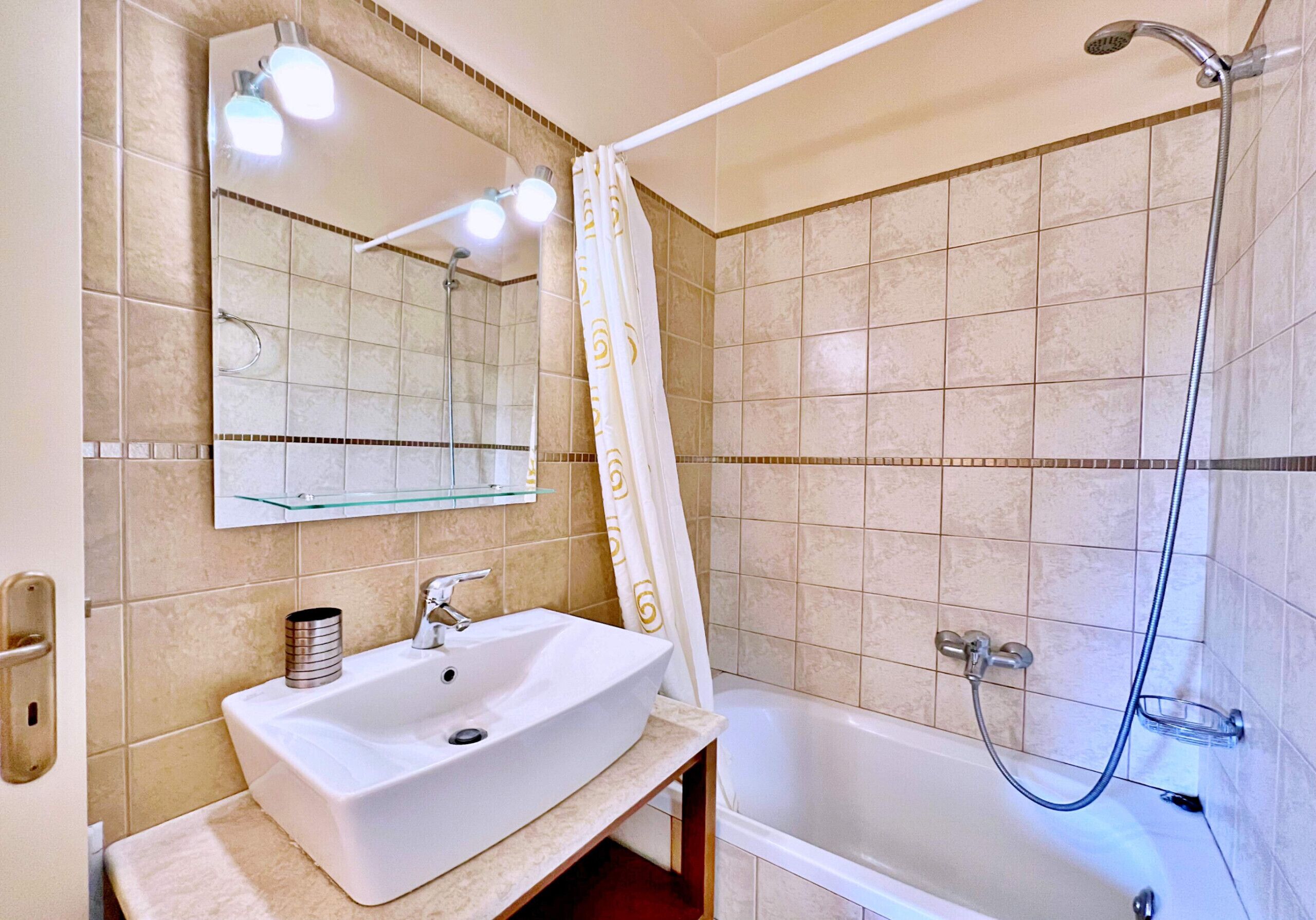 Een badkamer met een witte wastafel, een glazen plankje, een spiegel, een douche en een bad.