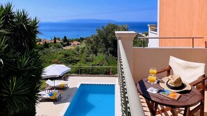 Vista a la piscina con una vista despejada del mar, una mesa con un sombrero y bebidas, y sillas de descanso.