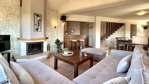 Een ruime woonkamer met een stenen open haard, een houten eettafel en een comfortabele zithoek.