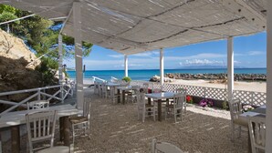 Un patio al aire libre con mesas y sillas, con vistas a una playa y al mar.