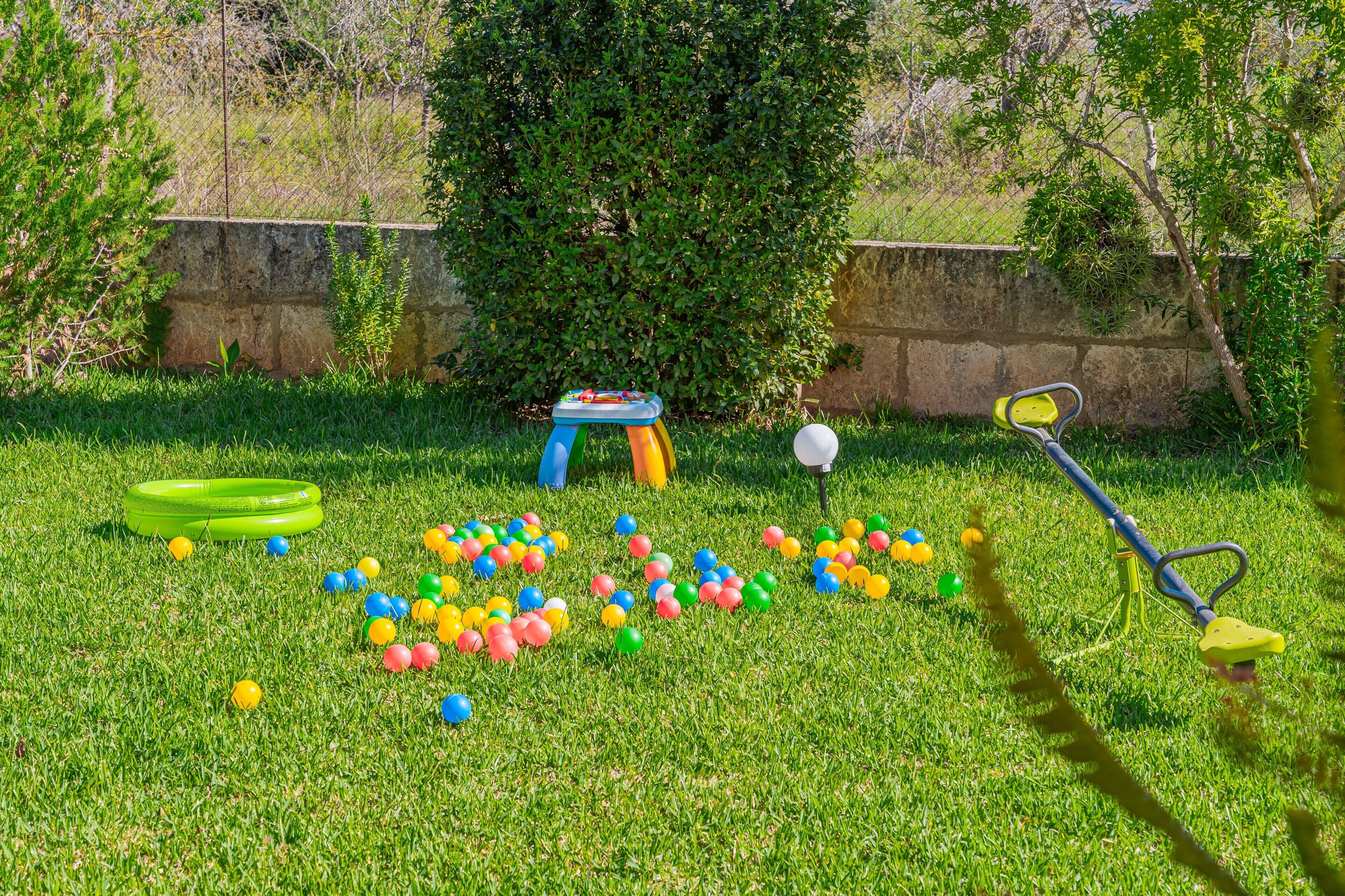 A grassy outdoor area with a trampoline, a small table, and a lawnmower.