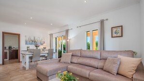 A modern living room with a beige sofa, a dining area, and a kitchen in the background. - Country Home “Son Serra” in Rural Area with Air Conditioning, Terrace & Garden (Buger)