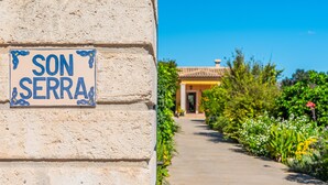 A stone wall with a sign reading 'SON SERRA' and a pathway leading to a building. - Country Home “Son Serra” in Rural Area with Air Conditioning, Terrace & Garden (Buger)