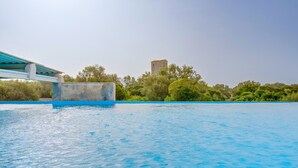 Ein Swimmingpool mit glatter, blauer Wasseroberfläche, ein Stein-Turm im Hintergrund und eine Brücke mit blauer Brüstung.