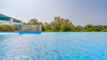 A swimming pool with a clear blue water surface, a stone tower in the background, and a bridge with a blue railing.