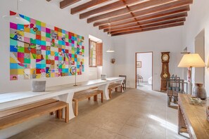 A spacious room with a long white bench, a colorful abstract painting, wooden beams, and a traditional clock. - Holiday Home "Casa del Señor" at Possessió Sa Barrala with Access to Es Trenc Beach (Campos)