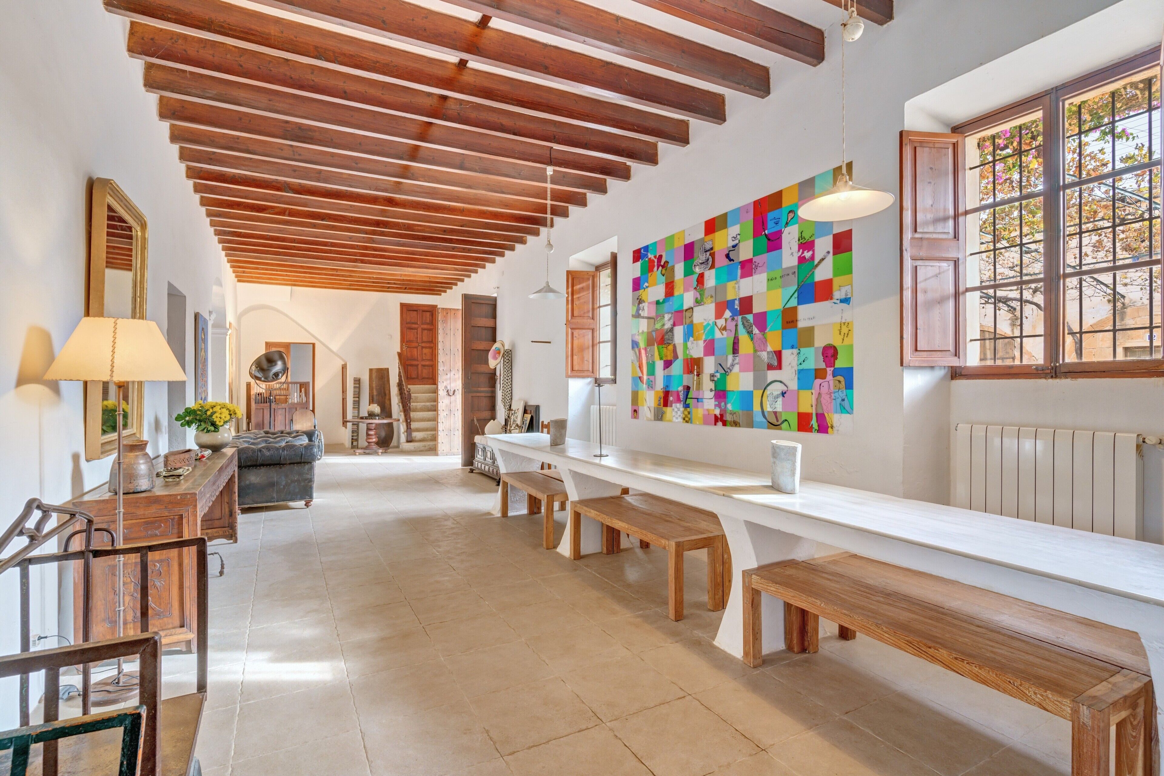 A spacious room with a wooden ceiling, a long white counter, wooden benches, and a colorful abstract painting on the wall.