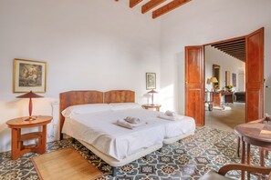 A bedroom with a large bed, two bedside tables, a wooden headboard, a patterned floor, and a mirror in the adjacent room. - Holiday Home "Casa del Señor" at Possessió Sa Barrala with Access to Es Trenc Beach (Campos)