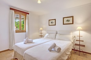 Une chambre d’hôtel avec deux lits, une fenêtre avec des rideaux, des lampes fixées au mur et deux tableaux encadrés.