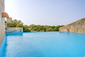 Une piscine avec un mur en pierre et de la verdure en arrière-plan.