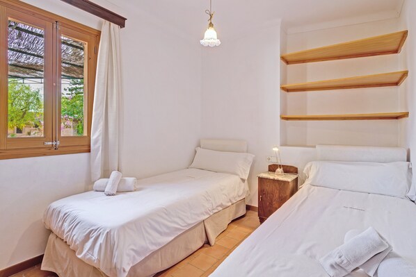 Une chambre avec deux lits, une fenêtre avec des rideaux, un luminaire suspendu et des étagères en bois.